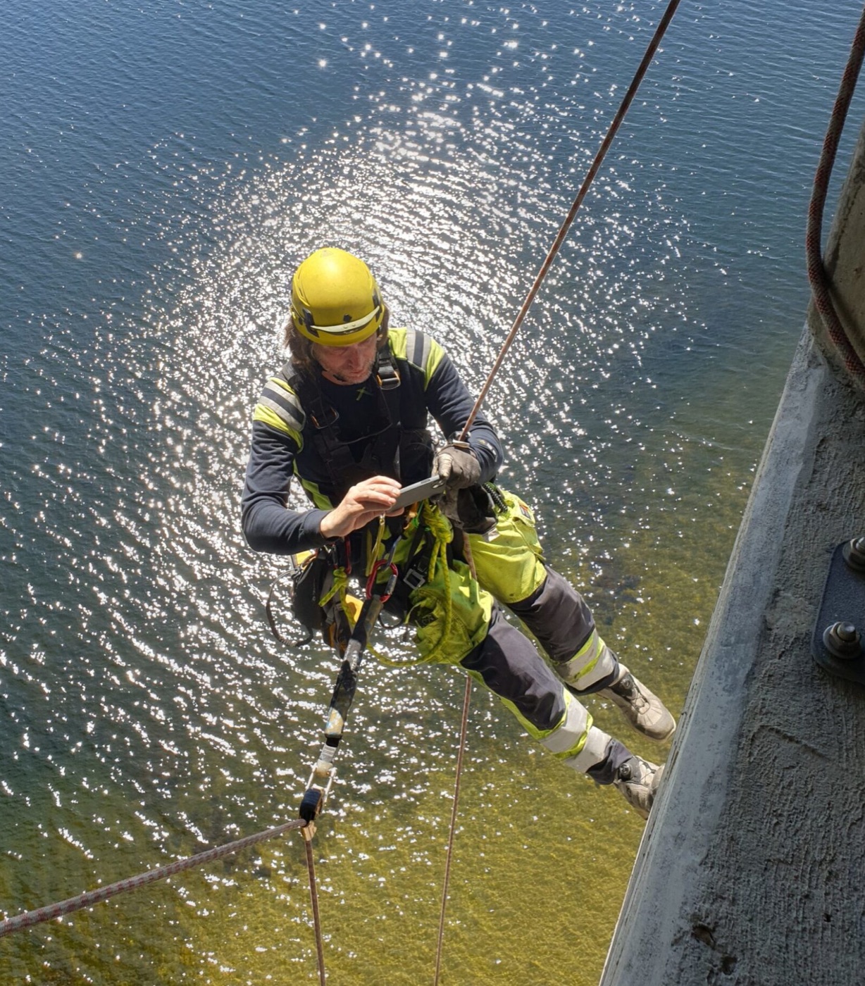 Technician checking a tablet while rigged over a bridge